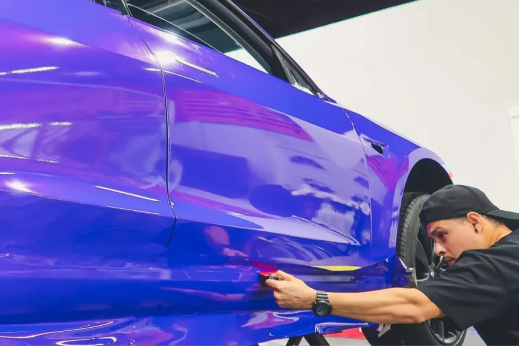 Close-up of vinyl wrap being applied to the side of a purple Tesla Model.
