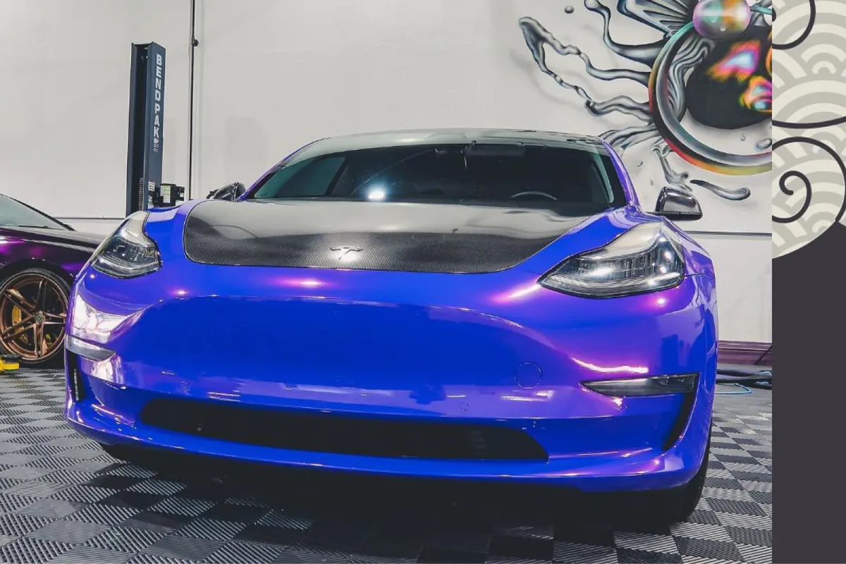 Purple Tesla Model with a carbon fiber hood in a garage.