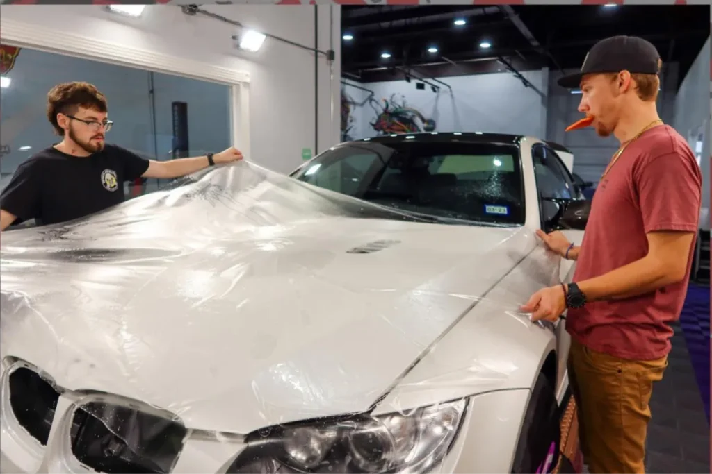 Two people applying paint protection film to the white BMW M3.
