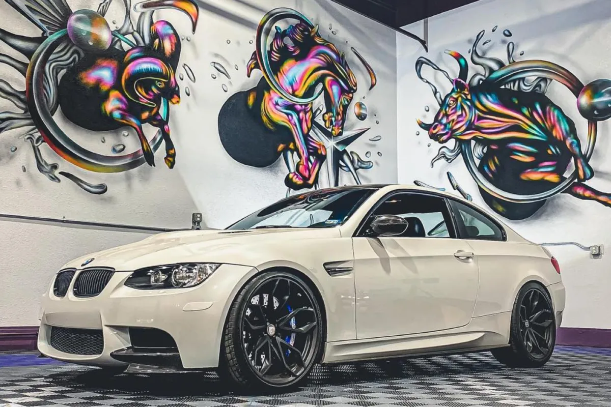 White BMW M3 with black wheels parked in front of vibrant graffiti.