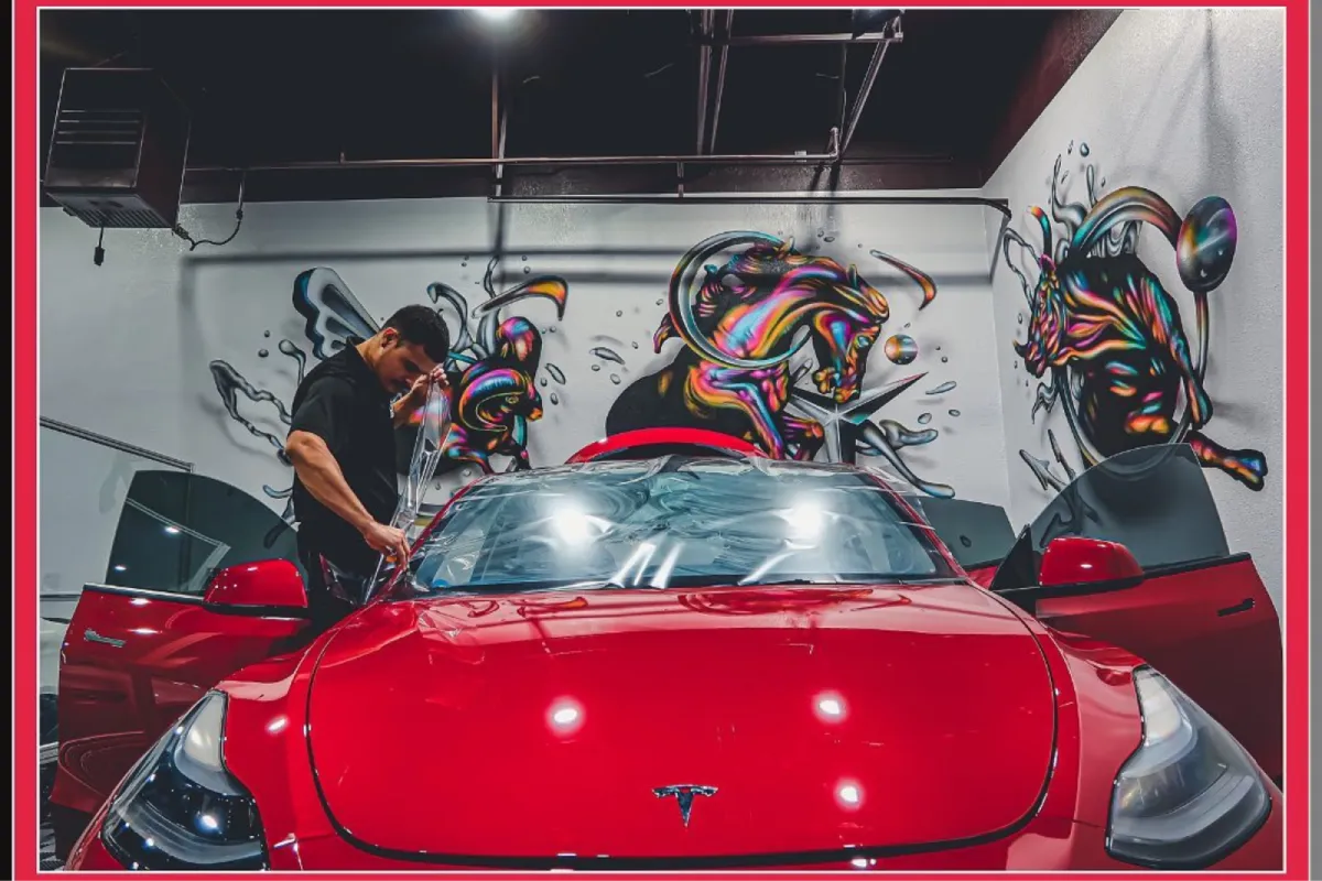 Technician applying window tint on a red Tesla in a tint shop.