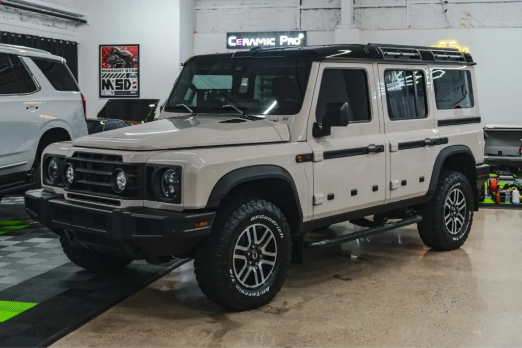 Beige off-road SUV in a workshop, showcasing upgraded suspension-style stance and aftermarket body kit installation details.