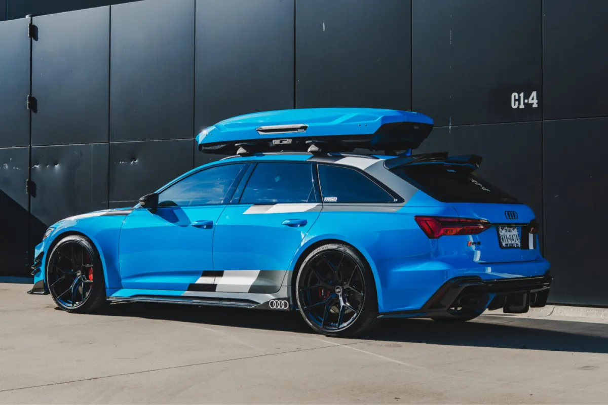 Blue performance SUV fitted with a roof-mounted cargo box and custom body kit, shown in a professional installation shop.
