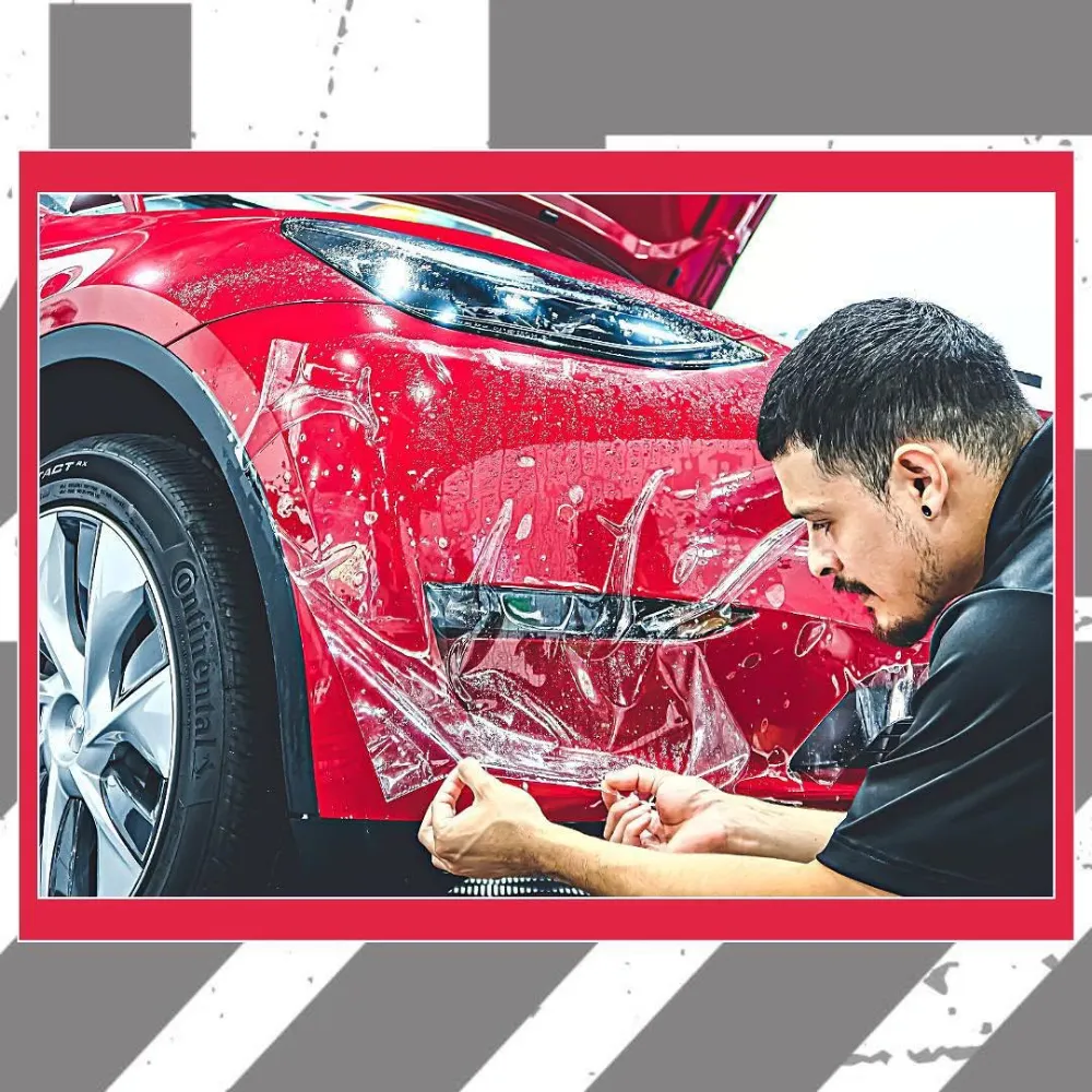 Technician applying clear paint protection film to the front bumper of a red car