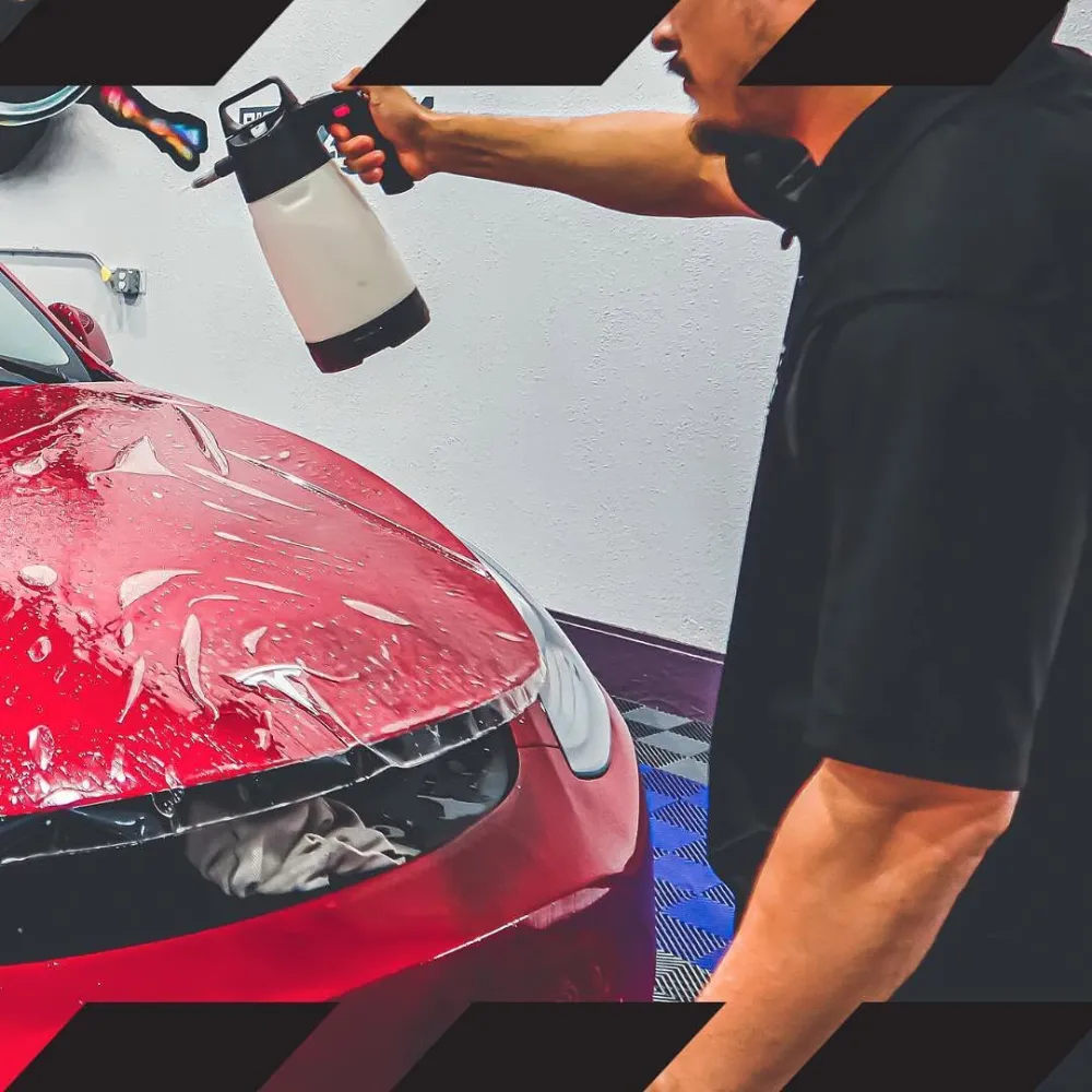 Detailer spraying solution while installing paint protection film on a red car hood